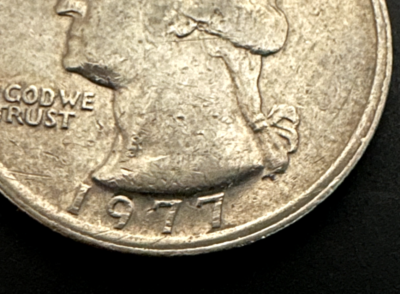 1977 quarter with dramatic off-center strike showing blank planchet visible and full date readable in the struck area